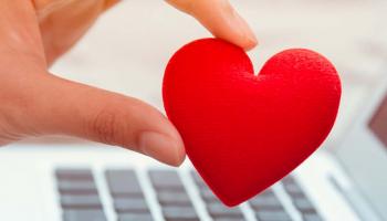 A hand holds a fabric heart over a laptop
